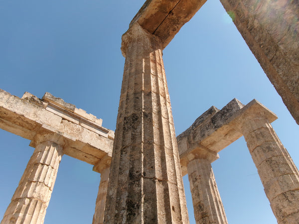 Ancient stone columns and ruins of a Greek or Roman temple structure under a clear blue sky.